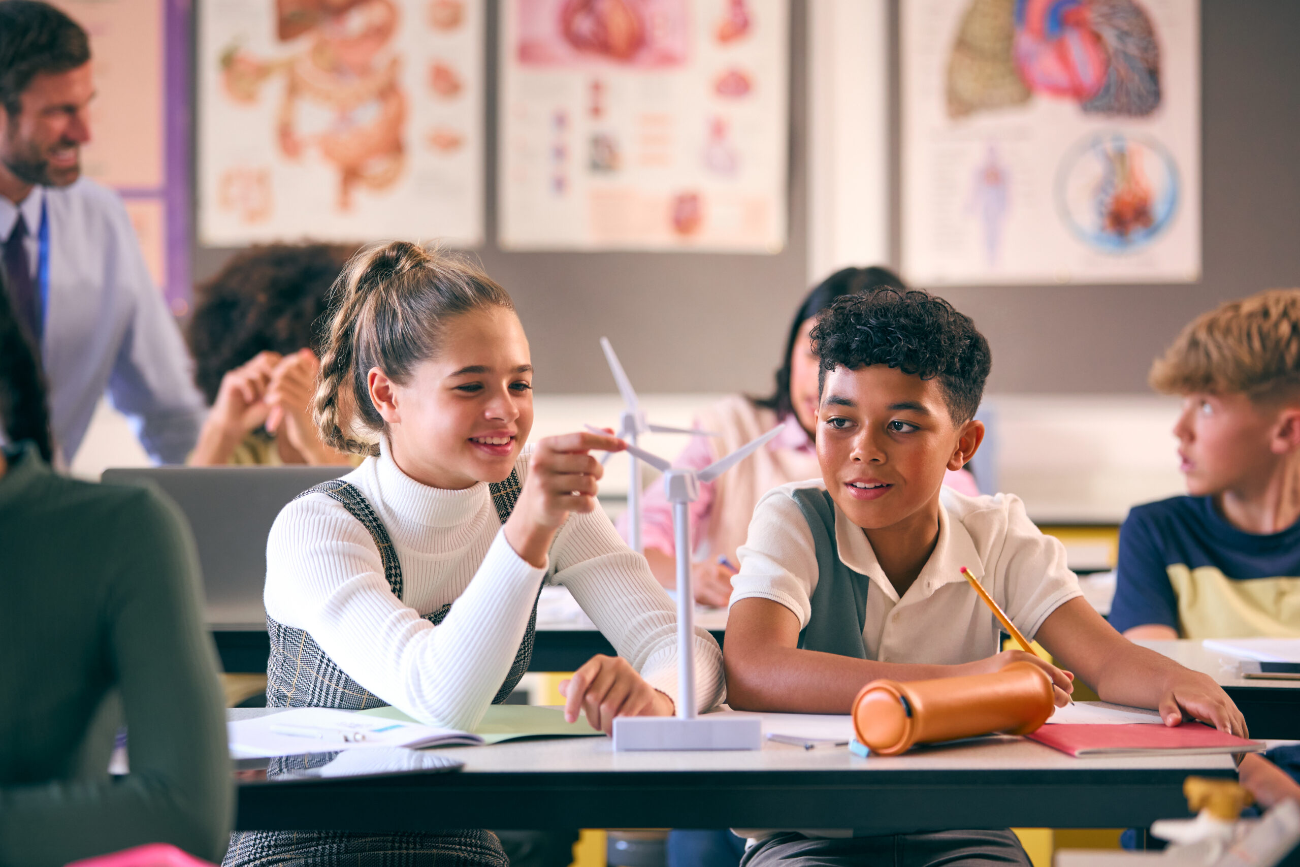 Secondary Or High School Students Studying Wind Turbines In Science Class With Teacher In Background